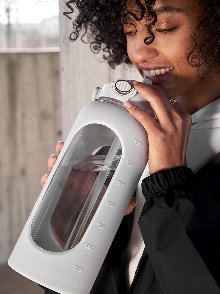 Ein Mädchen mit locken hält eine 2 Liter-´Trinkflasche und trinkt daraus. Die Flasche hat eine Strohhalm Funktion.