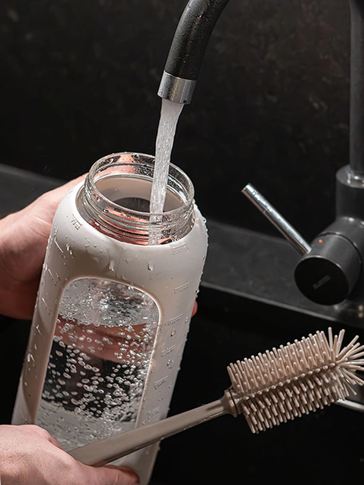 Person befüllt eine 2-Liter-Glasflasche mit großer Öffnung unter einem laufenden Wasserhahn. In der rechten Hand hält sie eine Flaschenbürste für die einfache Reinigung.