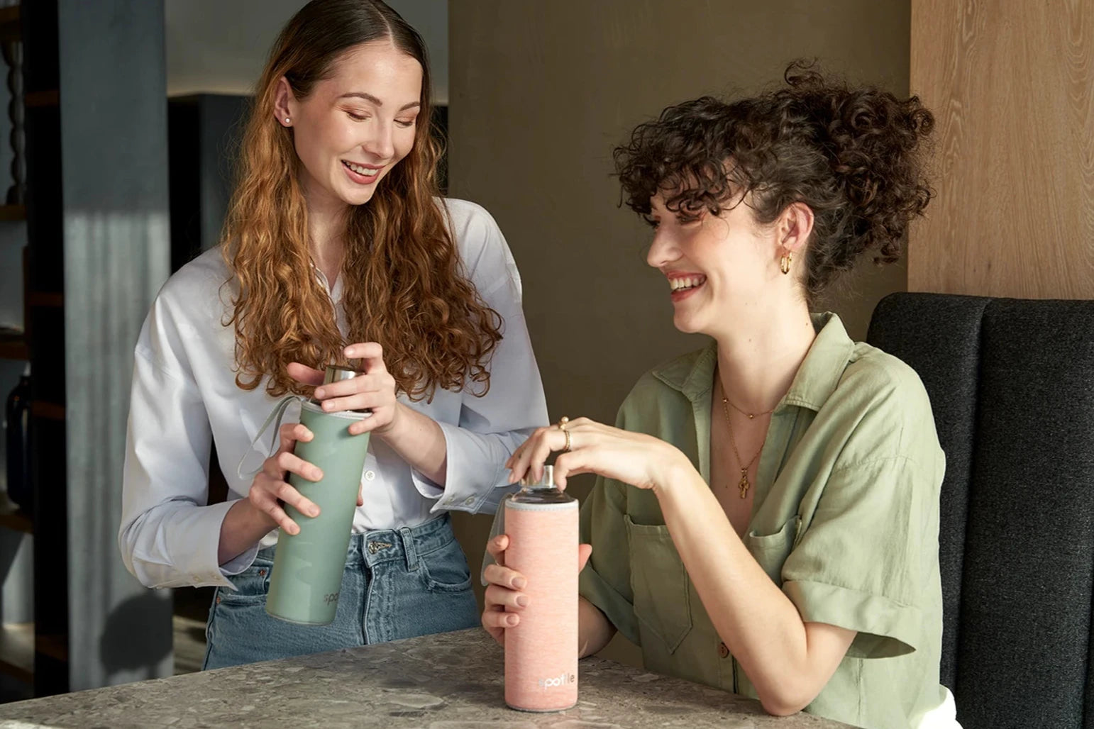 2 Mädchen, mit Trinkflaschen aus Glas, sitzen lächelt am Küchentisch.