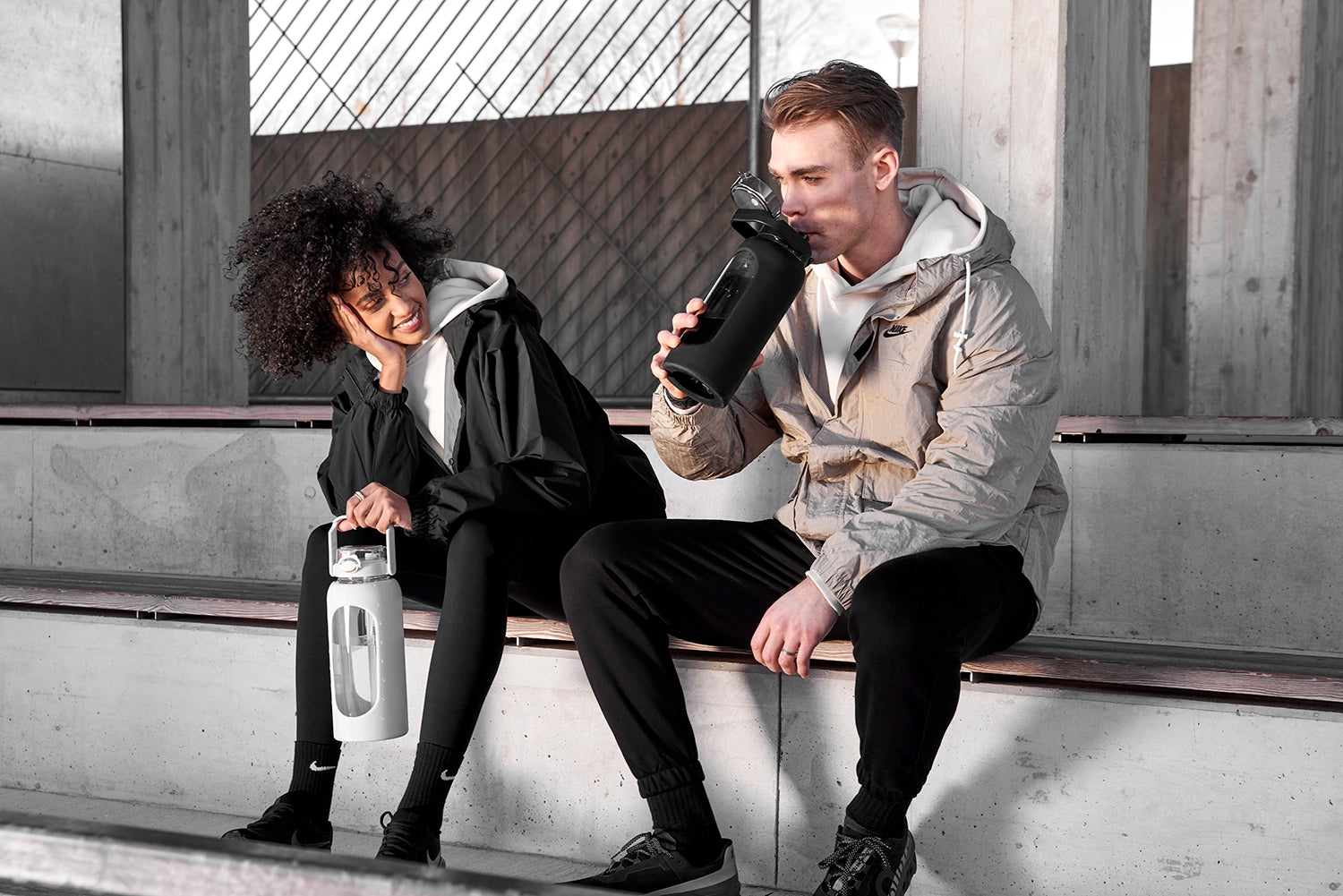 Ein Junge und ein Mädchen sitzen auf einer Bank im Freien und halten eine 2-Liter-Trinkflasche aus Glas mit Silikonhülle und integriertem Strohhalm.