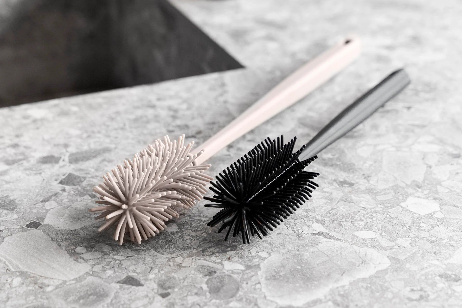 Verschiedenfarbige Silikon-Flaschenbürsten liegen auf einer hellen Arbeitsplatte in der Küche.