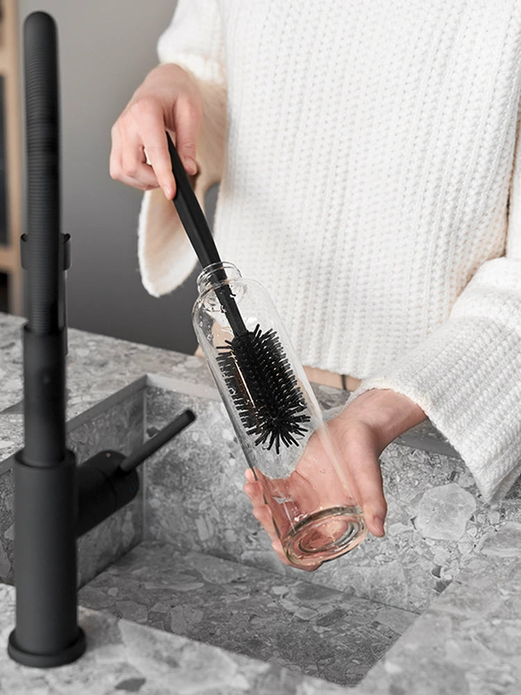 Schwarze Silikon-Reinigungsbürste reinigt eine Glasflasche. Die Bürste sieht hochwertig aus.