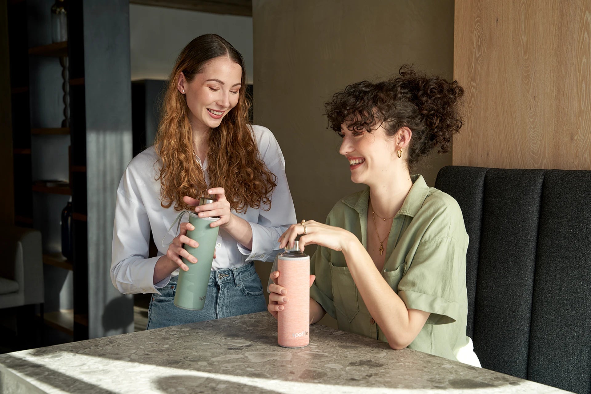 2 Mädchen, mit Trinkflaschen aus Glas, sitzen lächelt am Küchentisch.